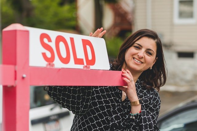 real estate agent holding a sold sign outside of a house